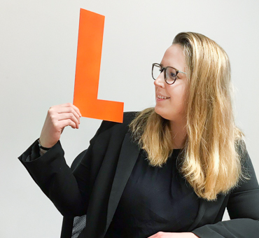 Person mit einem gebastelten Buchstaben L aus Pappe in der Hand.