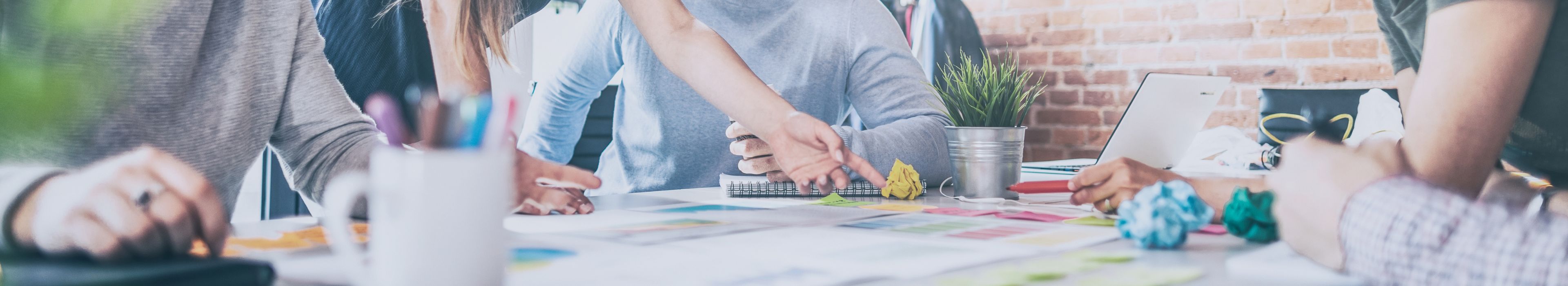 •	Nahaufnahme einer kreativen Brainstorming Runde, mit Händen, Dokumenten und Designmaterialien für Werbemittel- und Anzeigentests.
