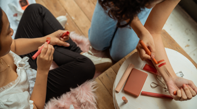 Produkttest: Zwei Frauen sitzen auf dem Boden und testen Make-up.