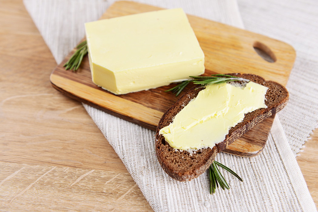 Alles in Butter? Wie Preispsychologie das Markenvertrauen im Handel beeinflusst Auf einem Holzbrett liegt ein Stück Butter neben einer Scheibe Roggenbrot, die frisch mit Butter bestrichen wurde