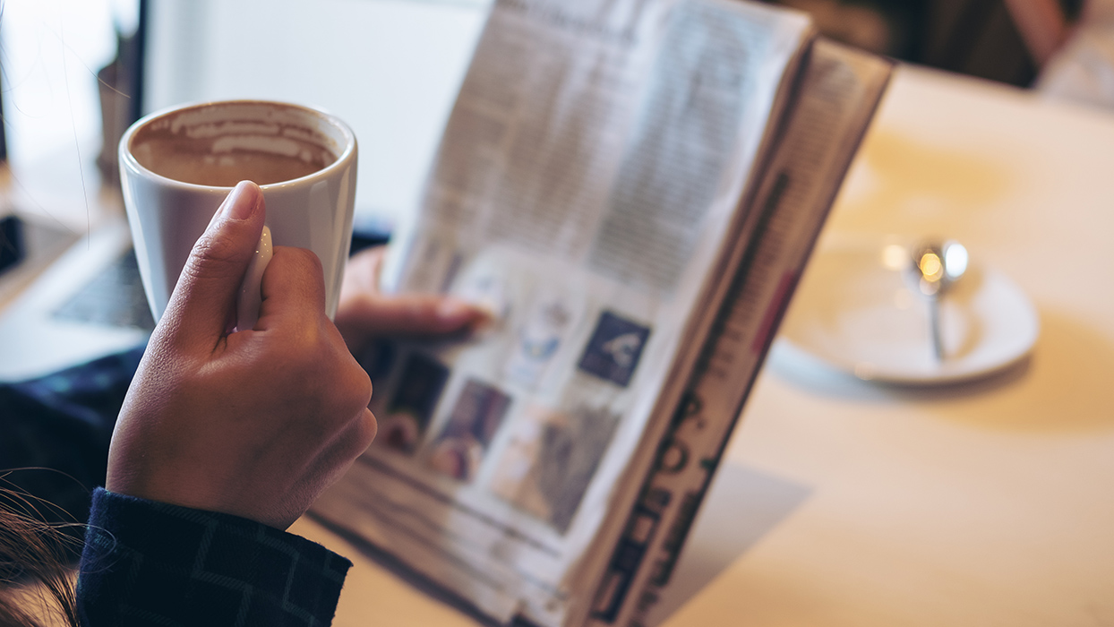 Frau hält eine Zeitung und eine Kaffeetasse in den Händen.
