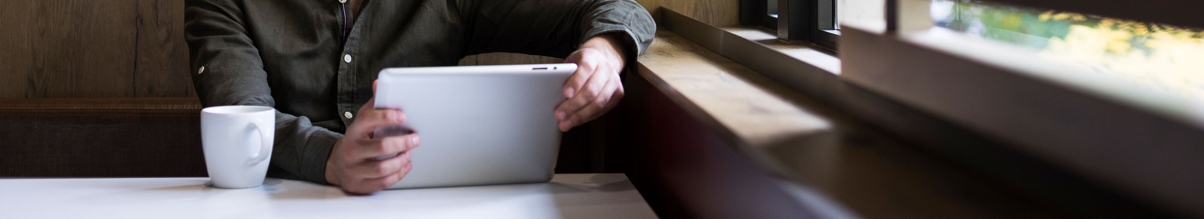 Person, die ein Tablet in der Hand hält und einen Arm gegen ein Fenstersims lehnt.