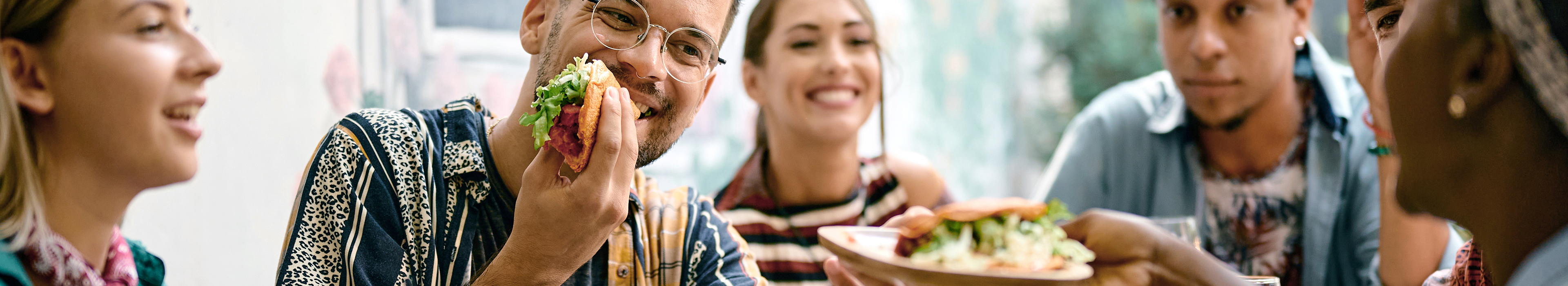 A group of young, happy people sit together at a table and share food.