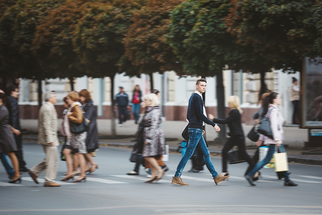Eine Gruppe von Menschen, die eine Straße überqueren, wobei ein Mann in der Mitte deutlich hervorsticht.