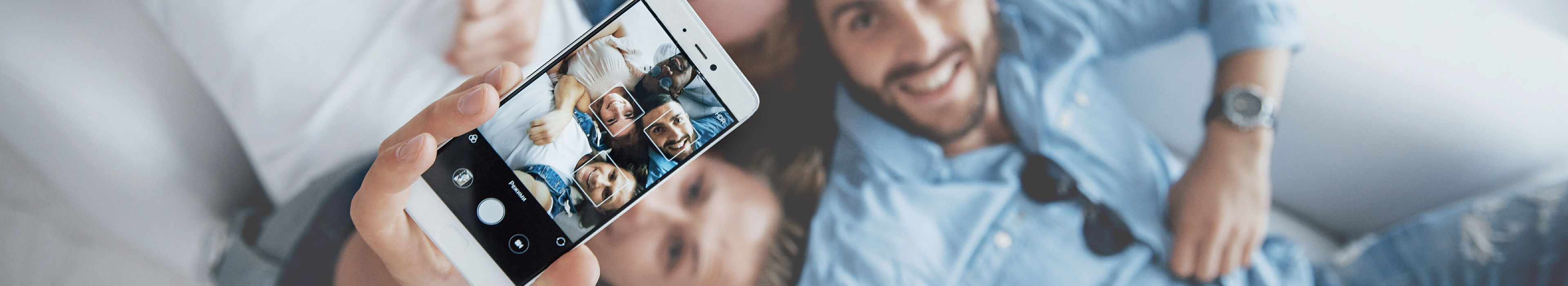 Fokus auf einem Smartphone, mit dem ein Selfie von drei Personen gemacht wird.