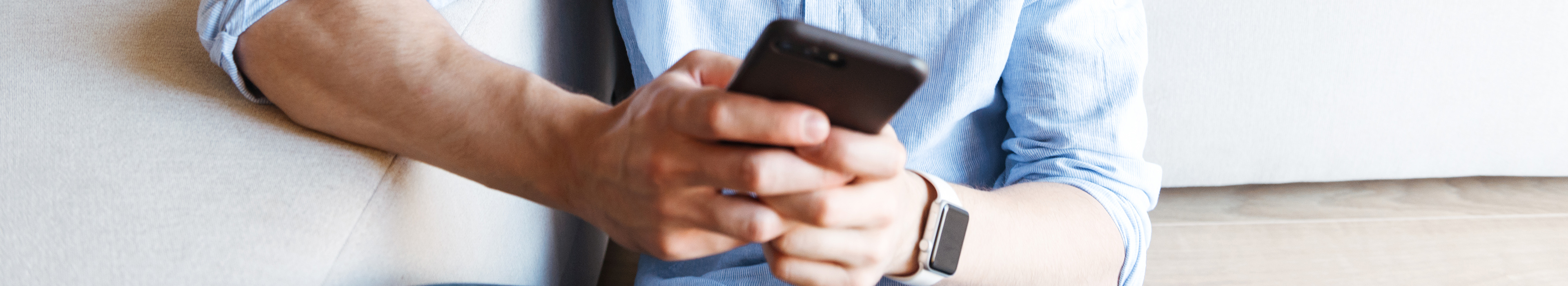 Ein Mann sitzt vor einem Sofa und hält ein Smartphone in den Händen. 