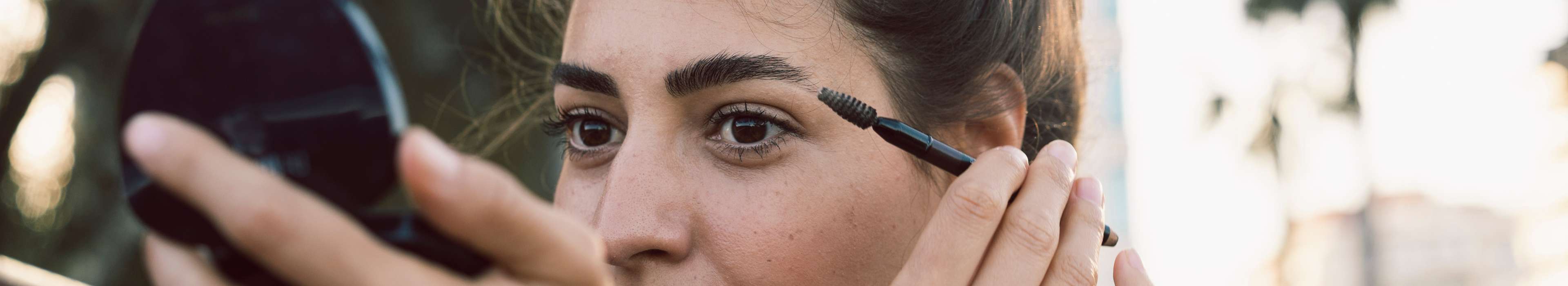 Eine Frau schaut in einen Kosmetik-Handspiegel und nutzt ein Beauty-Produkt.