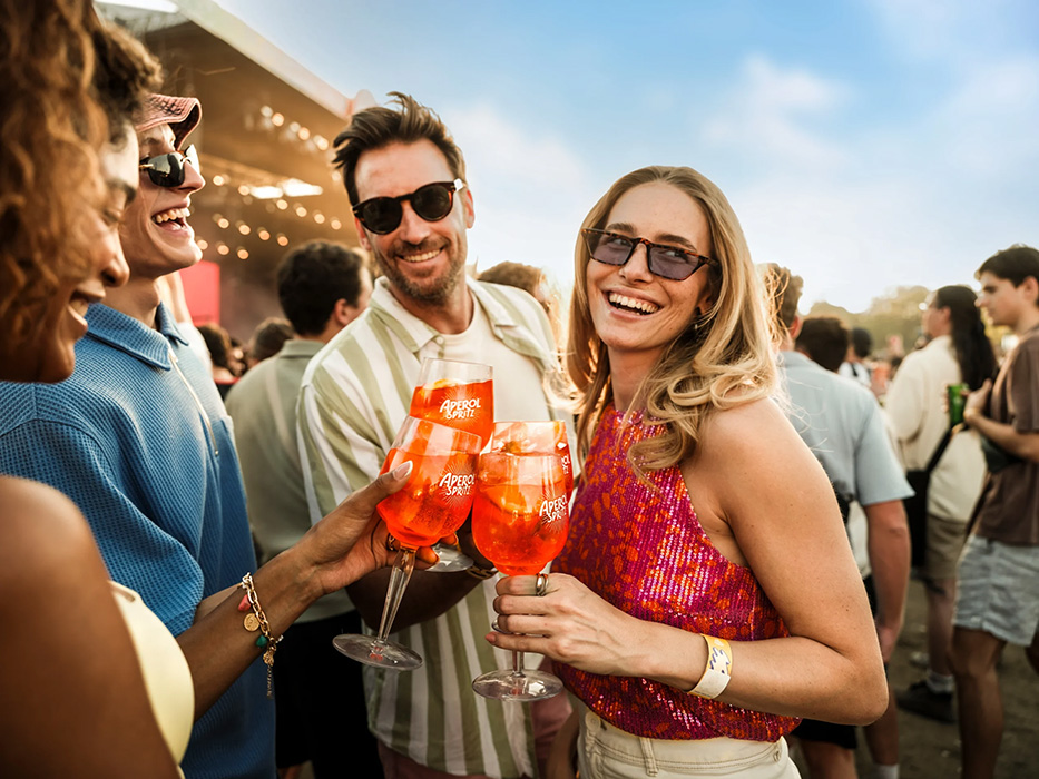 Gruppe von Menschen stößt bei einem Open-Air-Event mit Aperol-Spritz-Gläsern an.