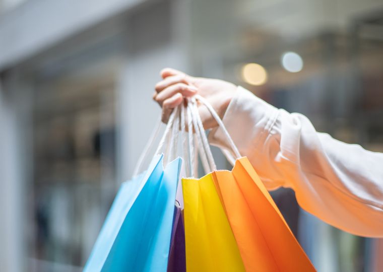 Mehrere bunte Einkaufs-Tüten werden von einer Hand hochgehalten.