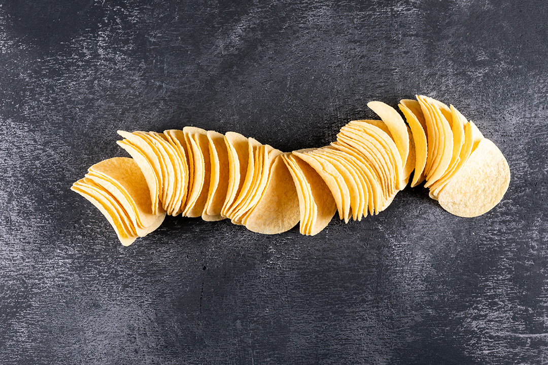 Eine lange, geschwungene Reihe dünner, gleichmäßig geformter Kartoffelchips auf einer dunklen, strukturierten Oberfläche.