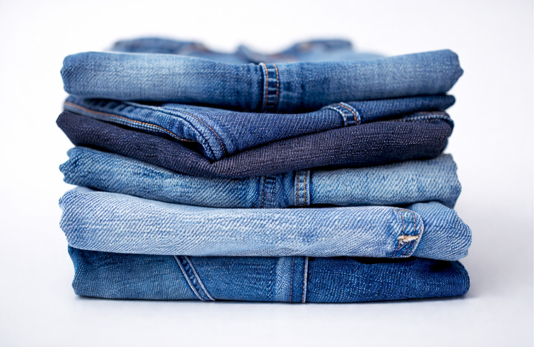 Weißer Hintergrund mit einem Stapel Jeanshosen in der Mitte.