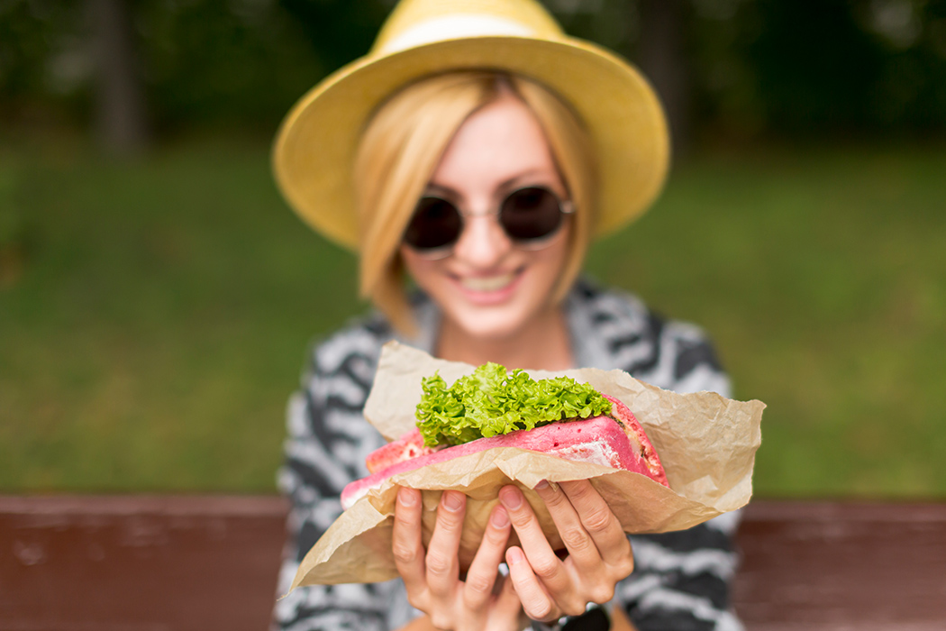 Lächelnde Frau mit einem Sandwich in den Händen.