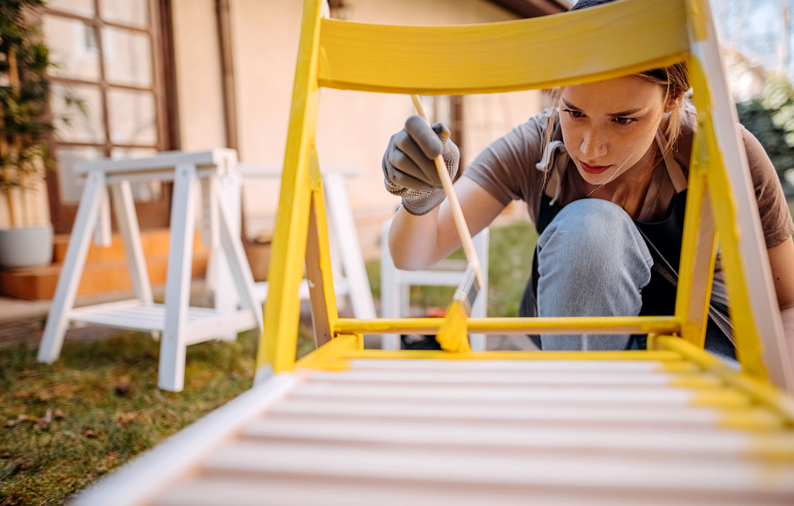 Person, die mit gelber Farbe Gartenmöbel bemalt.